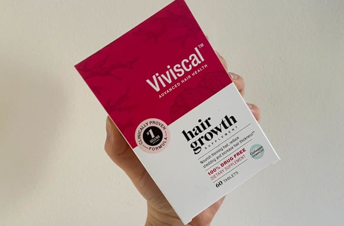 A person holding a box of Viviscal Hair Growth supplement against a white background.